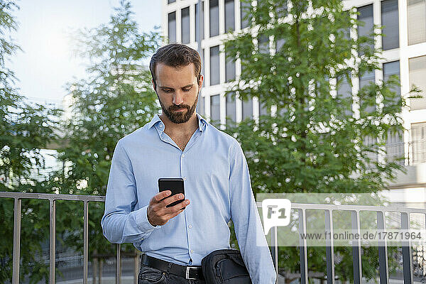 Young businessman using smart phone standing in front of trees