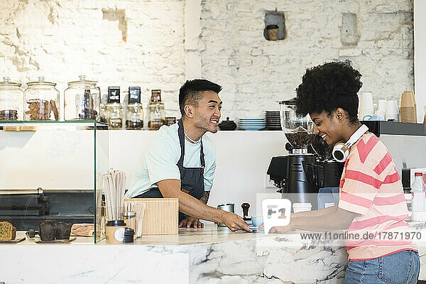 Smiling man serving coffee to customer in cafe