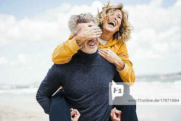 Fröhliche Frau bedeckt die Augen eines Mannes mit der Hand am Strand