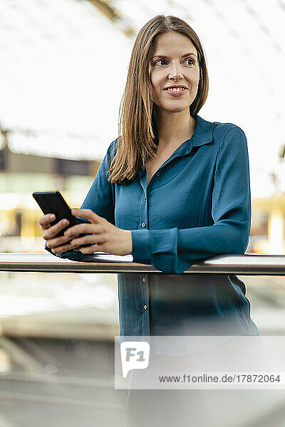 Smiling businesswoman with smart phone in office corridor