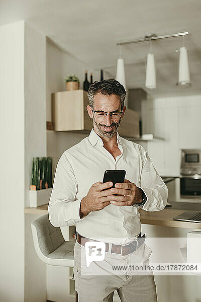 Lächelnder Geschäftsmann  der zu Hause sein Mobiltelefon benutzt