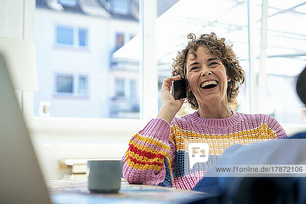 Cheerful woman talking on smart phone sitting at home
