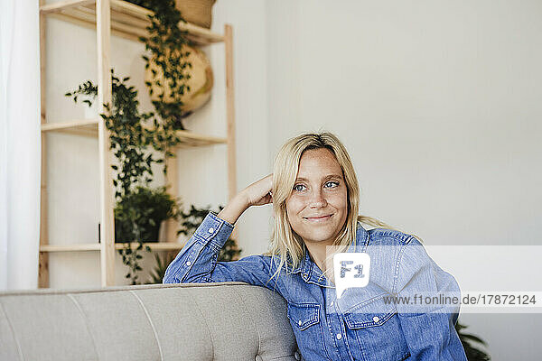 Contemplative young blond woman relaxing on sofa at home