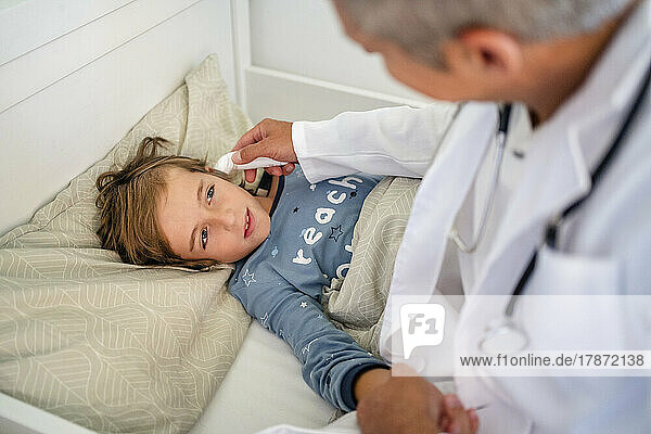 Doctor examining boy in bed at home