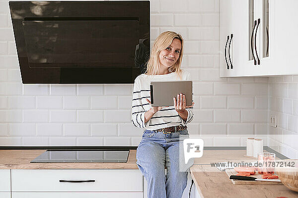 Smiling woman with tablet PC on kitchen counter at home
