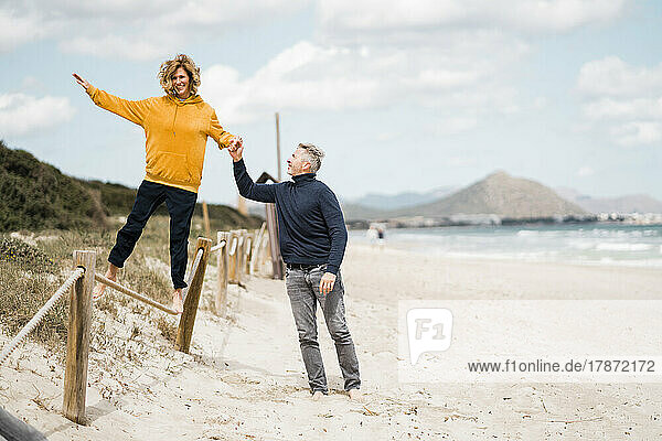 Happy mature man with woman walking on rope at beach