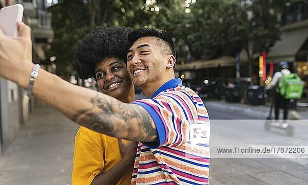 Smiling young man taking selfie on smart phone with woman