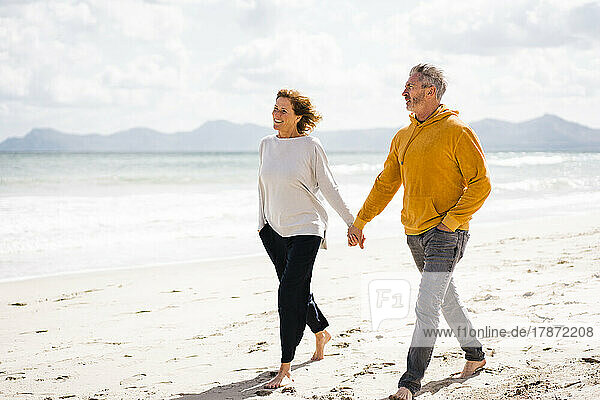 Glückliches Paar  das an einem sonnigen Tag Händchen haltend am Ufer spaziert