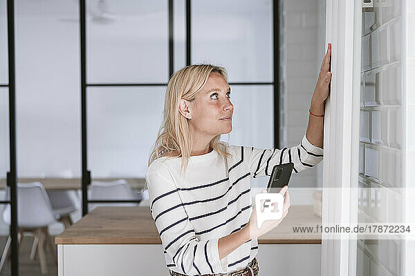 Woman with smart phone touching radiator at home