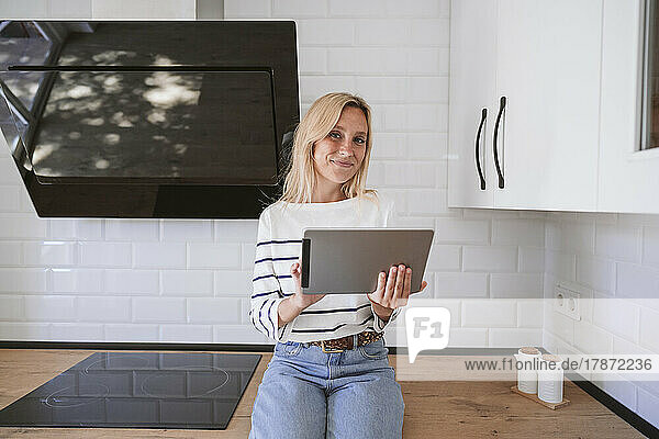 Smiling woman holding tablet PC on kitchen counter at home