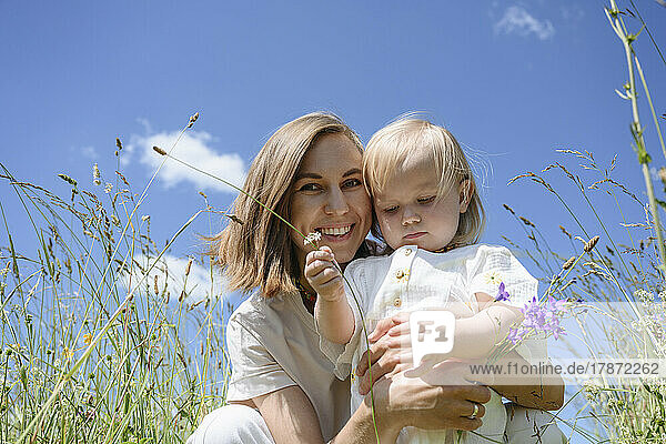 Happy mother with daughter sitting under sky at field