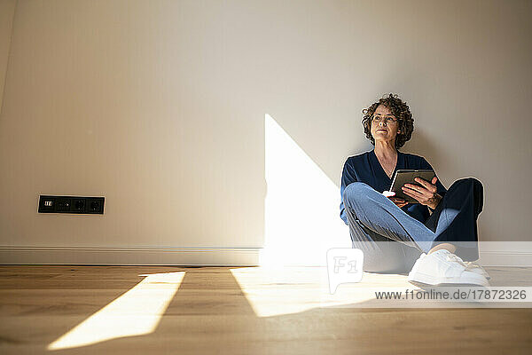 Thoughtful real estate agent with tablet PC sitting on floor at home