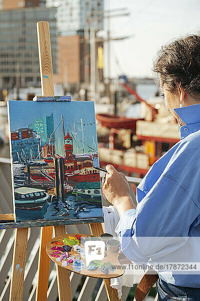 Female painter holding palette painting on canvas at harbor