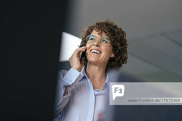 Glückliche Geschäftsfrau mit Brille  die im Büro auf dem Smartphone spricht