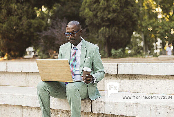 Businessman with coffee cup using laptop in park