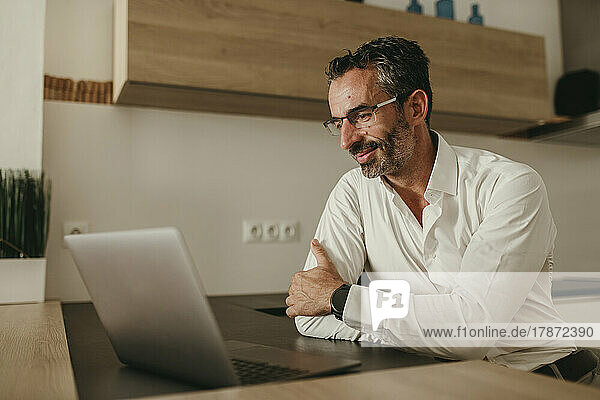 Mature businessman looking at laptop in kitchen