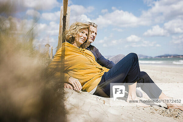 Happy mature man with woman sitting at beach on sunny day
