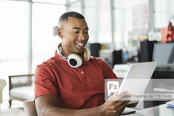 Smiling businessman with wireless headphones using tablet PC in office