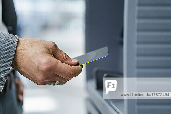 Hand of businessman holding credit card near ATM machine