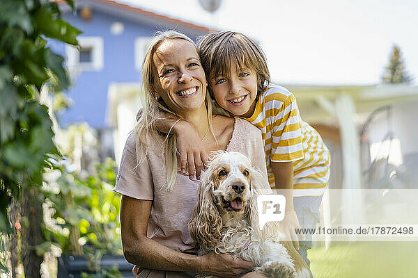 Porträt einer lächelnden Mutter und ihres Sohnes mit Hund im Garten