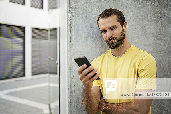Junger junger Mann mit Bart benutzt Mobiltelefon und steht vor der Wand