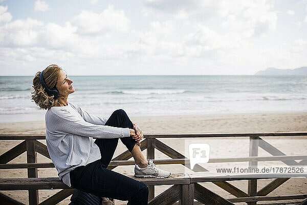 Happy woman wearing wireless headphones listening music at beach