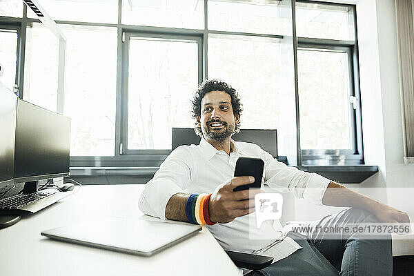 Smiling businessman with smart phone by desk at office