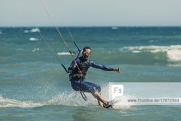 Man wearing wetsuit kiteboarding in sea on sunny day