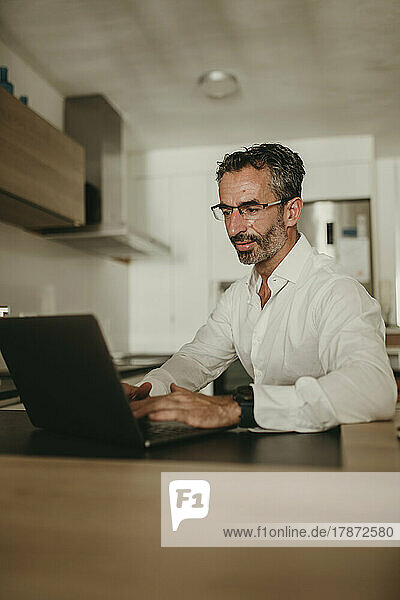Mature businessman using laptop on kitchen counter at home