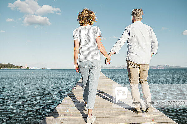 Mature couple holding hands walking on jetty