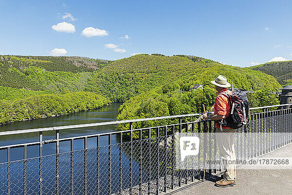 Senior man wearing hat and backpack standing by railing looking at view  Eifel National Park  Germany