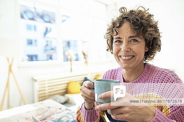 Smiling woman with curly hair holding coffee cup at home