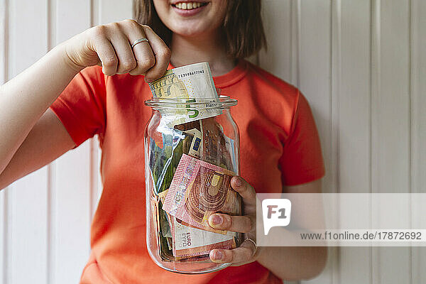 Girl removing five Euro banknote from glass jar