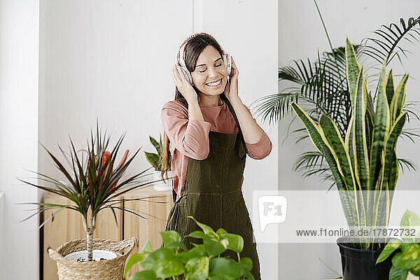 Happy woman listening music through headphones standing by plants at home