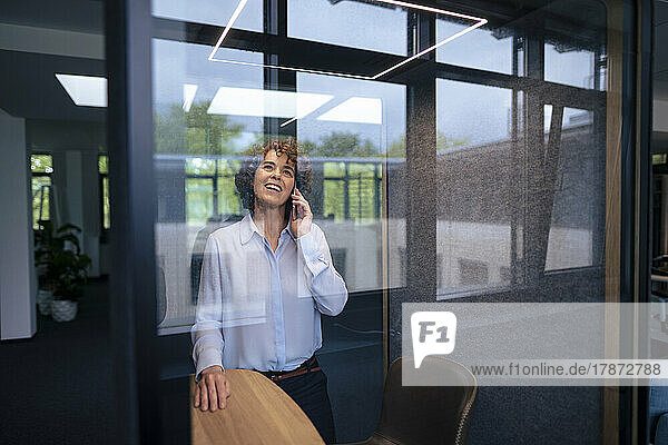 Happy businesswoman talking through mobile phone in soundproof cabin
