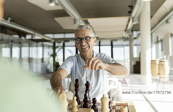 Happy mature businessman playing chess with colleague in office