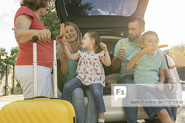 Happy family eating ice pops sitting at back of car