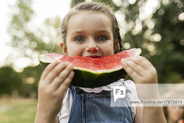 Cute girl eating watermelon standing at park