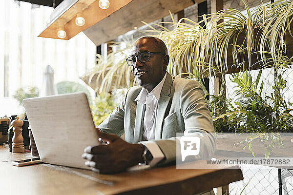 Smiling businessman using laptop at table in cafe