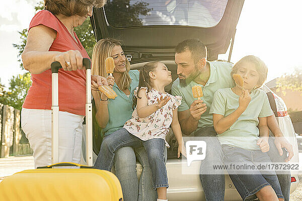 Smiling family eating ice pops sitting in car trunk
