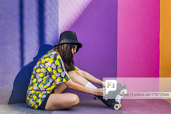 Woman wearing hat tying shoelace on roller skate by multi colored wall