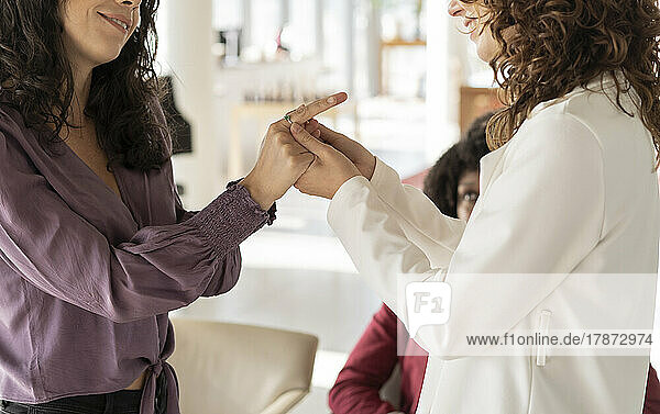 Lächelnde Geschäftsfrauen halten Händchen und trösten sich gegenseitig im Büro