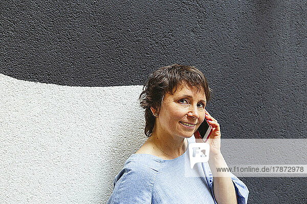 Reife Frau telefoniert an der Wand mit dem Handy
