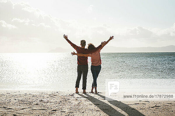 Carefree couple with arms outstretched standing on shore at beach
