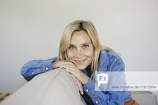 Smiling blond woman sitting on sofa at home