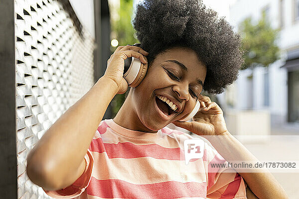 Fröhliche junge Frau mit geschlossenen Augen  die über kabellose Kopfhörer Musik hört