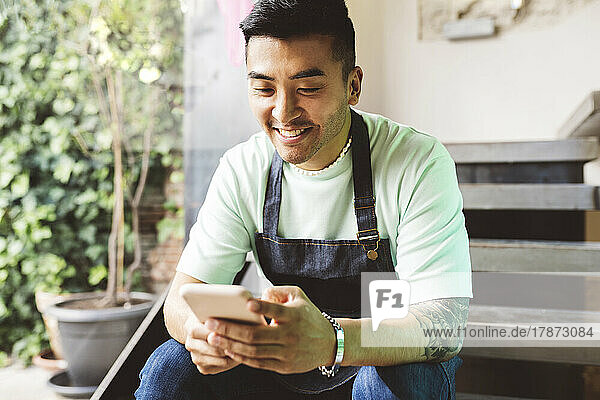 Glücklicher Mann  der sein Mobiltelefon benutzt und auf Stufen im Café sitzt