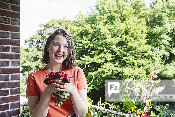 Happy girl holding fresh radishes on balcony