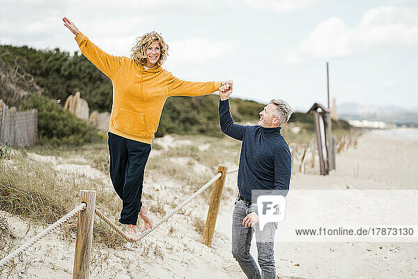 Carefree woman walking on rope with support of man at beach
