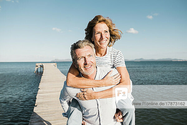 Happy man giving piggyback ride to woman on jetty